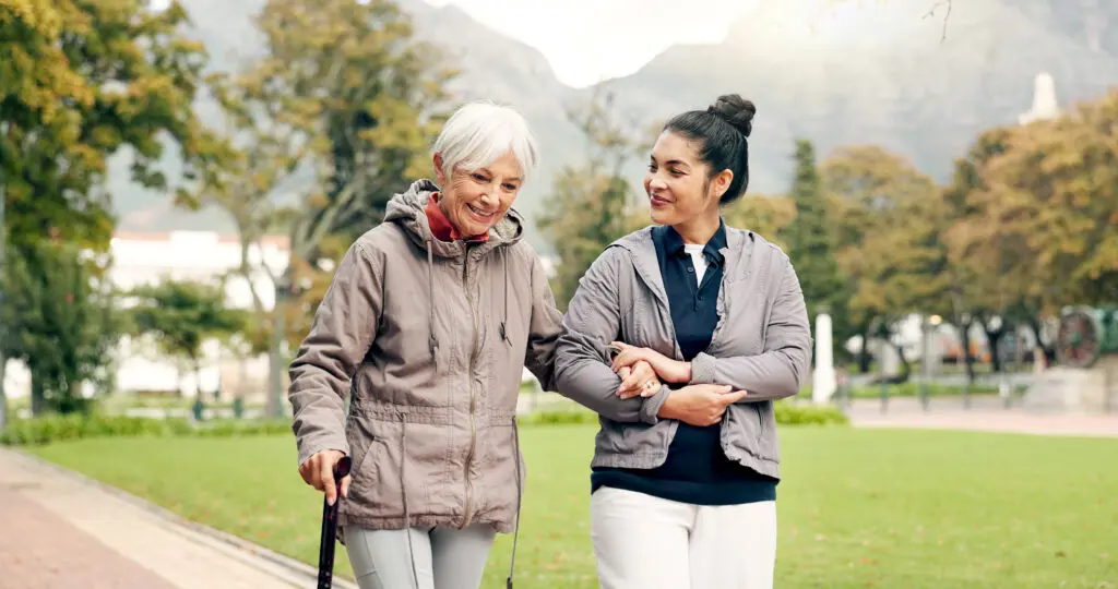 senior woman walking with help of another woman while talking about signs for Assisted Living at Burcham Hills in East Lansing, MI