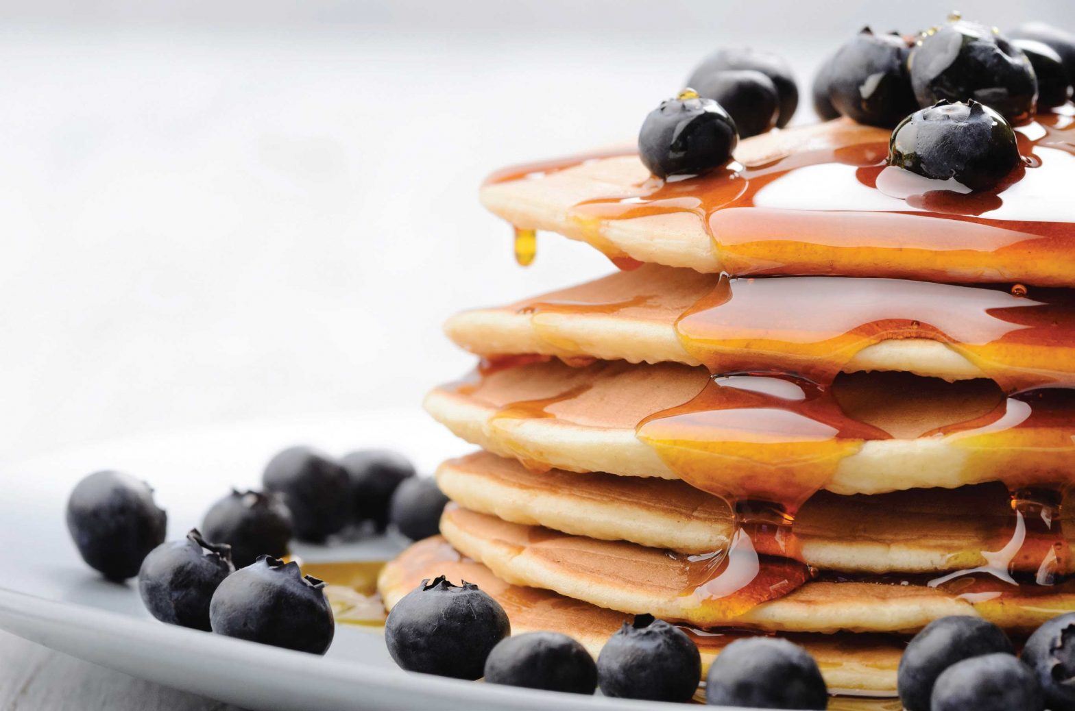 a stack of pancakes that are drizzled with maple syrup and fresh blueberries