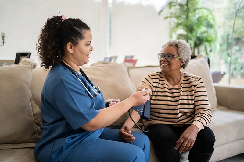 senior woman getting blood pressure taken by female nurse and talkings about signs for Assisted Living at Burcham Hills in East Lansing, MI