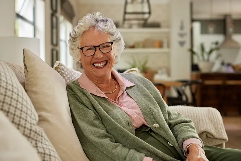 A senior woman smiling in her home in Lansing, MI while thinking about senior living buy-in vs monthly rent communities like Burcham Hills.