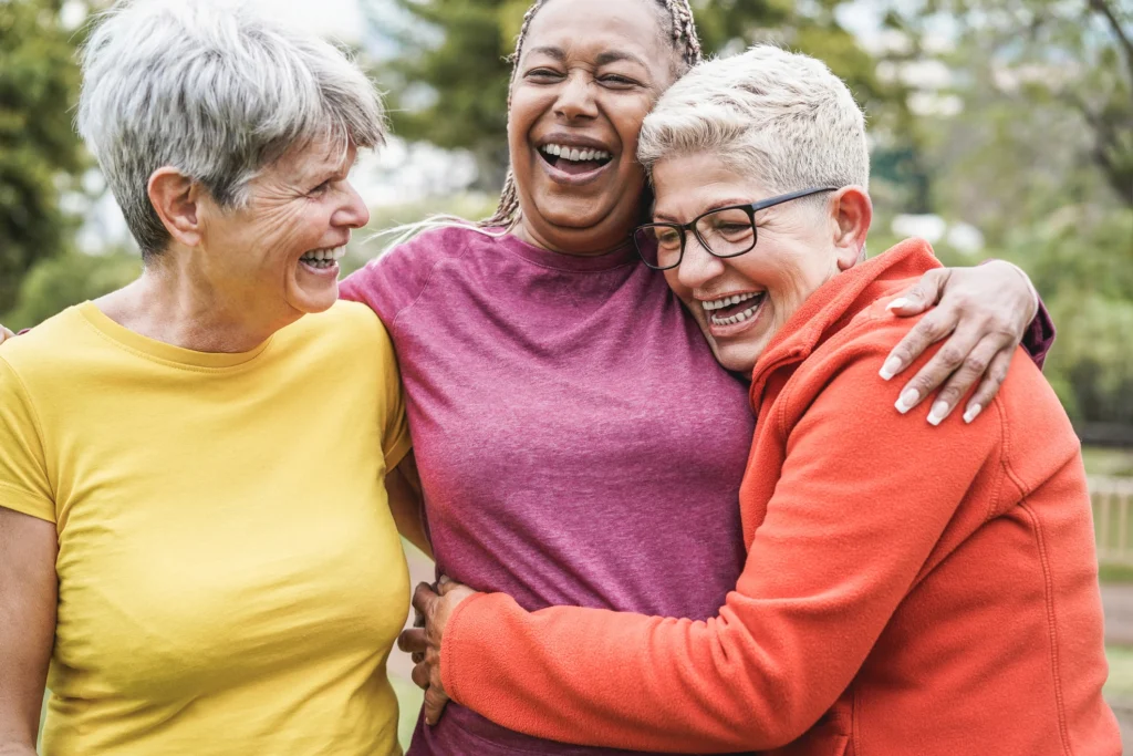 Three senior women smiling and laughing after discussing the benefits of "what is a CCRC" at Burcham Hills, a life plan community in East Lansing, MI.